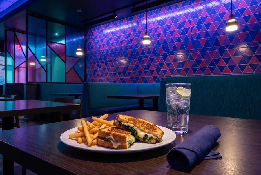 Generated picture: a toasted sandwich with fries and a glass of sparkling water on a dark table, teal booths and a wall of coloured triangle tiles behind.